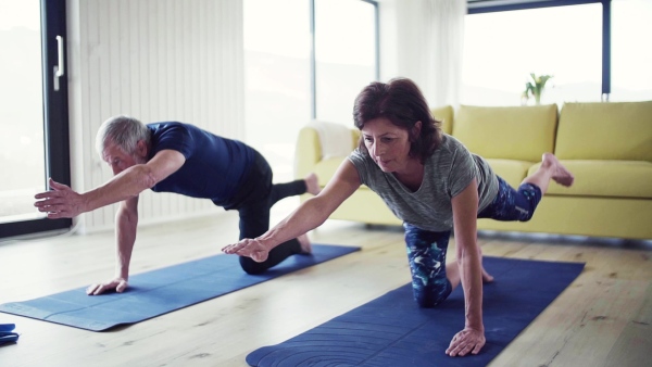 A happy senior couple indoors at home, doing exercise indoors. Slow motion.