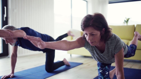 A happy senior couple indoors at home, doing exercise indoors. Slow motion.