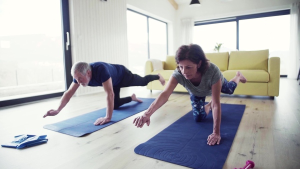 A happy senior couple indoors at home, doing exercise indoors. Slow motion.