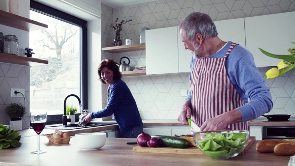 A portrait of happy senior couple indoors at home, cooking. Slow motion.