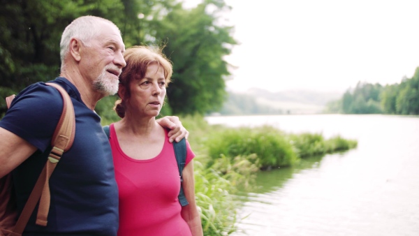 A senior tourist couple on a walk in nature, standing by lake.