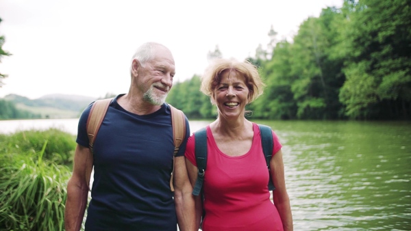 A senior tourist couple on a walk in nature, standing by lake. Slow motion.