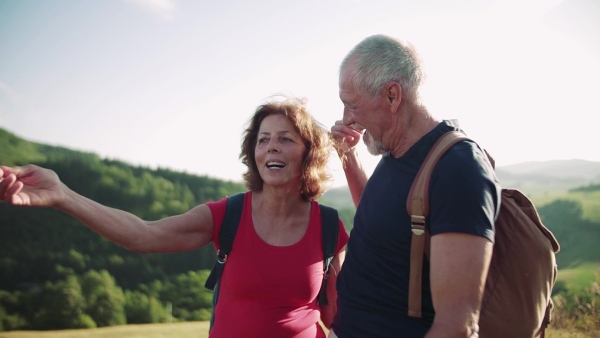 Senior tourist couple travellers with backpacks hiking in nature, resting and talking. Slow motion.