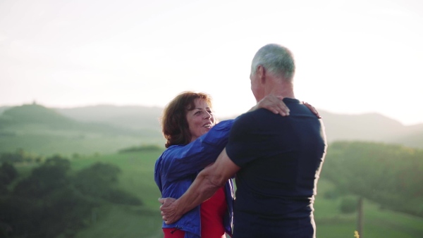 Senior tourist couple travellers hiking in nature, hugging when resting. Slow motion.