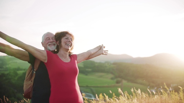 Senior tourist couple travellers with arms stretched hiking in nature, resting. Slow motion.