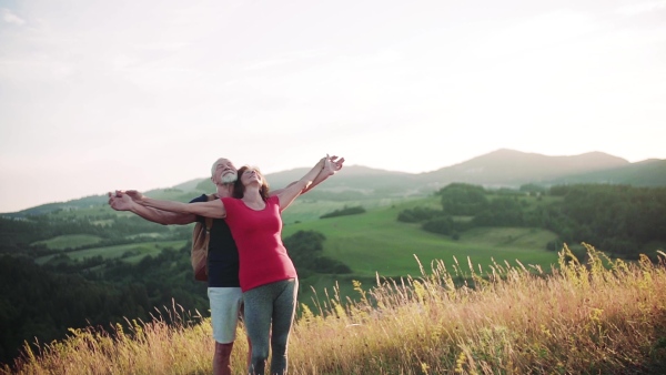 Senior tourist couple travellers with arms stretched hiking in nature, resting. Slow motion.