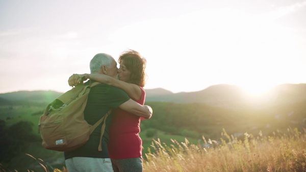 Senior tourist couple travellers hiking in nature, kissing when resting. Slow motion.