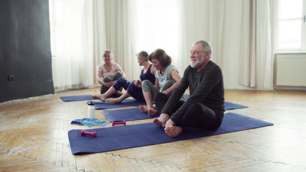 Group of active senior people doing yoga exercise in community center club.