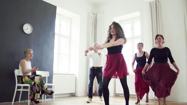 A group of senior people attending dancing class with dance teacher.