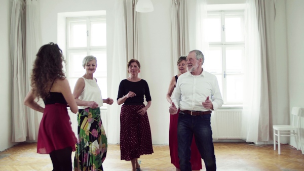 A group of senior people attending dancing class with dance teacher.