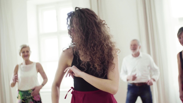 A group of senior people attending dancing class with dance teacher.