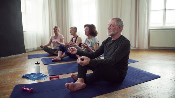 Group of active senior people doing yoga exercise in community center club. Slow motion.