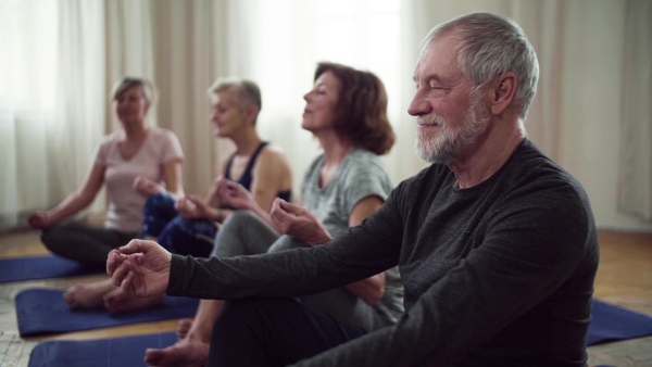 Group of active senior people doing yoga exercise in community center club. Slow motion.