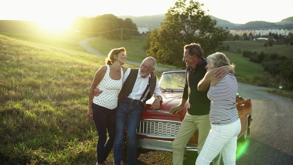 Two senior couples standing by cabriolet on a road trip in summer, talking. Slow motion.