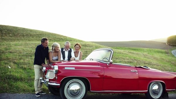 Two senior couples standing by cabriolet on a road trip in summer, looking at the map and planning. Slow motion.