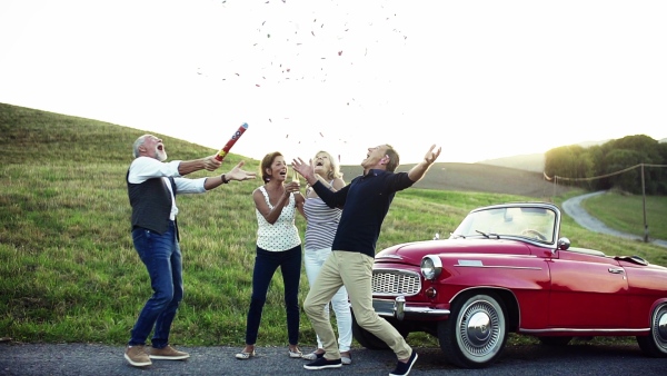 Two senior couples standing by cabriolet on a road trip in summer, having fun. Slow motion.