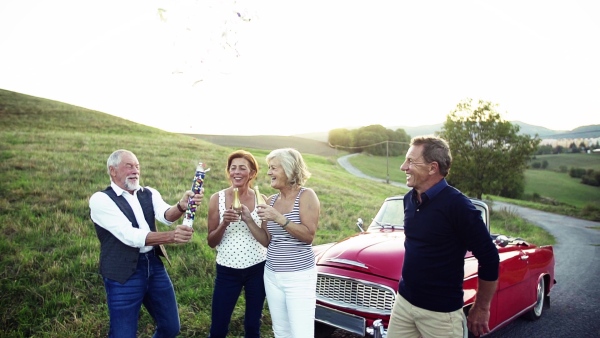 Two senior couples standing by cabriolet on a road trip in summer, having fun. Slow motion.