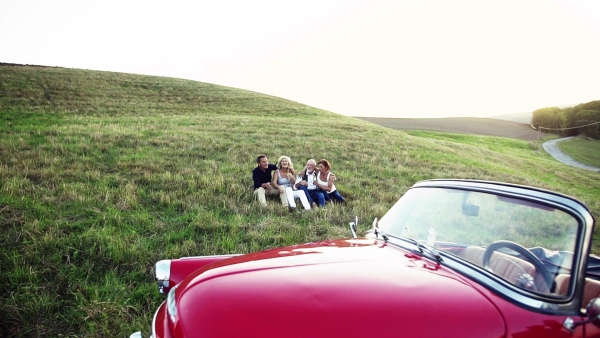 Two senior couples sitting by cabriolet on a road trip in summer, talking. Slow motion.