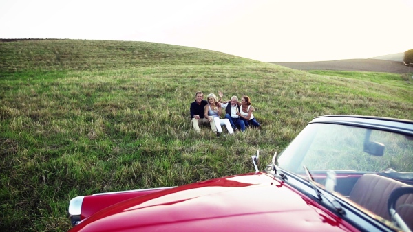 Two senior couples sitting by cabriolet on a road trip in summer, talking. Slow motion.