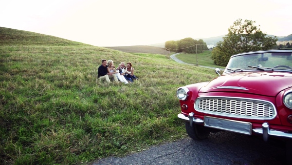 Two senior couples sitting by cabriolet on a road trip in summer, talking. Slow motion.