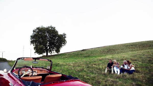 Two senior couples sitting by cabriolet on a road trip in summer, talking. Slow motion.