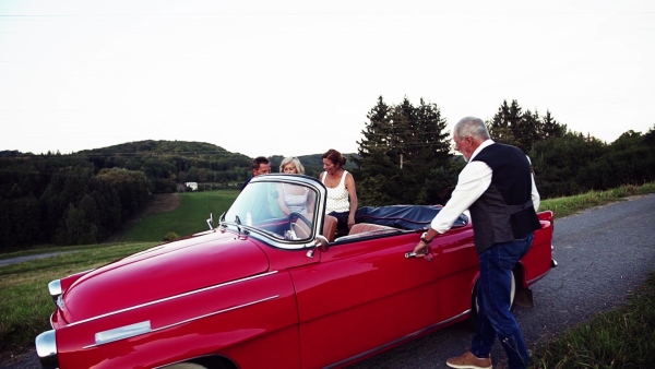 Two senior couples getting in cabriolet on a road trip in summer. Slow motion.