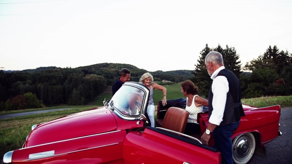 Two senior couples with cabriolet on a road trip in summer, laughing. Slow motion.