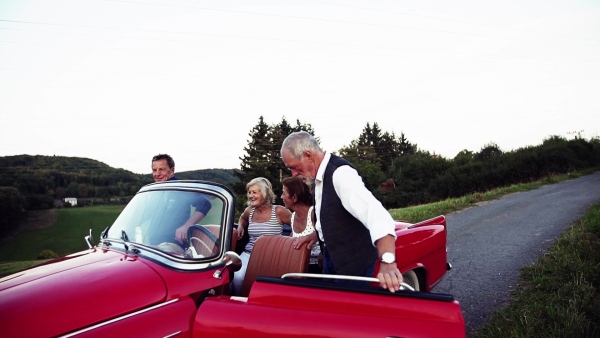 Two senior couples getting in cabriolet on a road trip in summer. Slow motion.