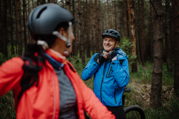 A senior couple bikers putting on cycling helmet outdoors in forest in autumn day.