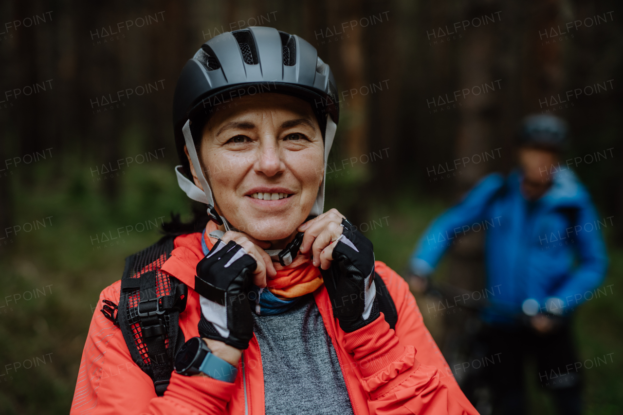 A senior couple bikers putting on cycling helmet outdoors in forest in autumn day, lookin at camera