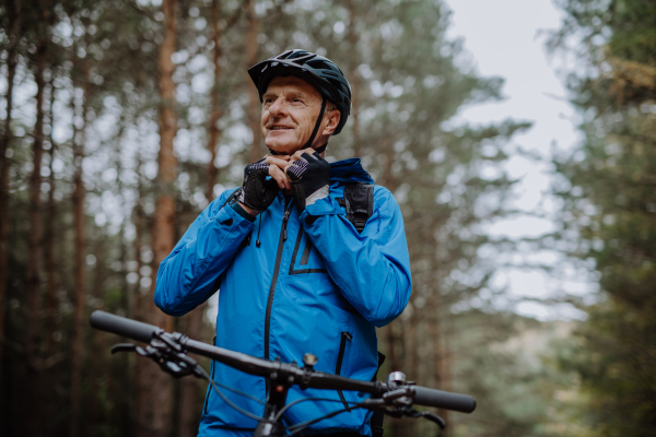 A n active senior man biker standing with bike outdoors in forest in autumn day.