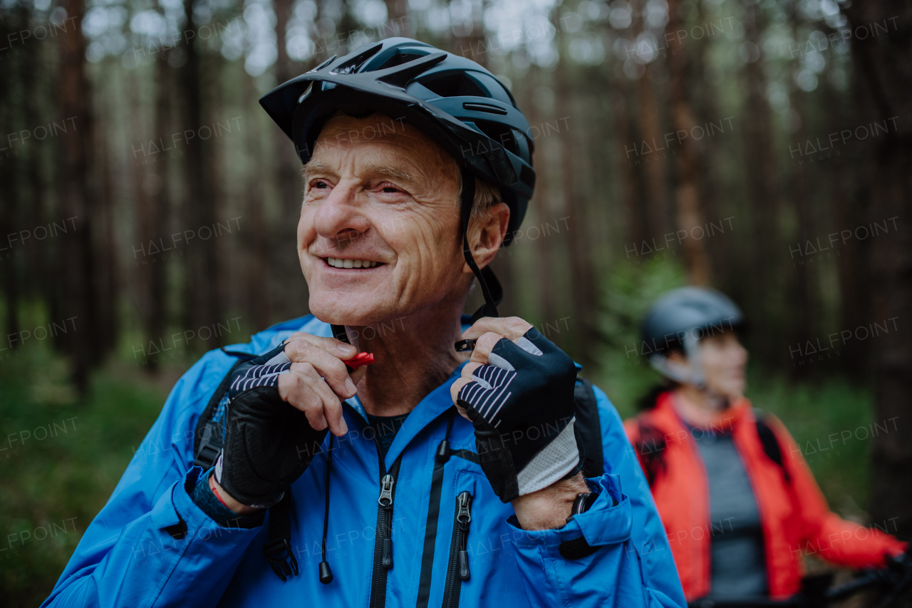 A senior couple bikers putting on cycling helmet outdoors in forest in autumn day.