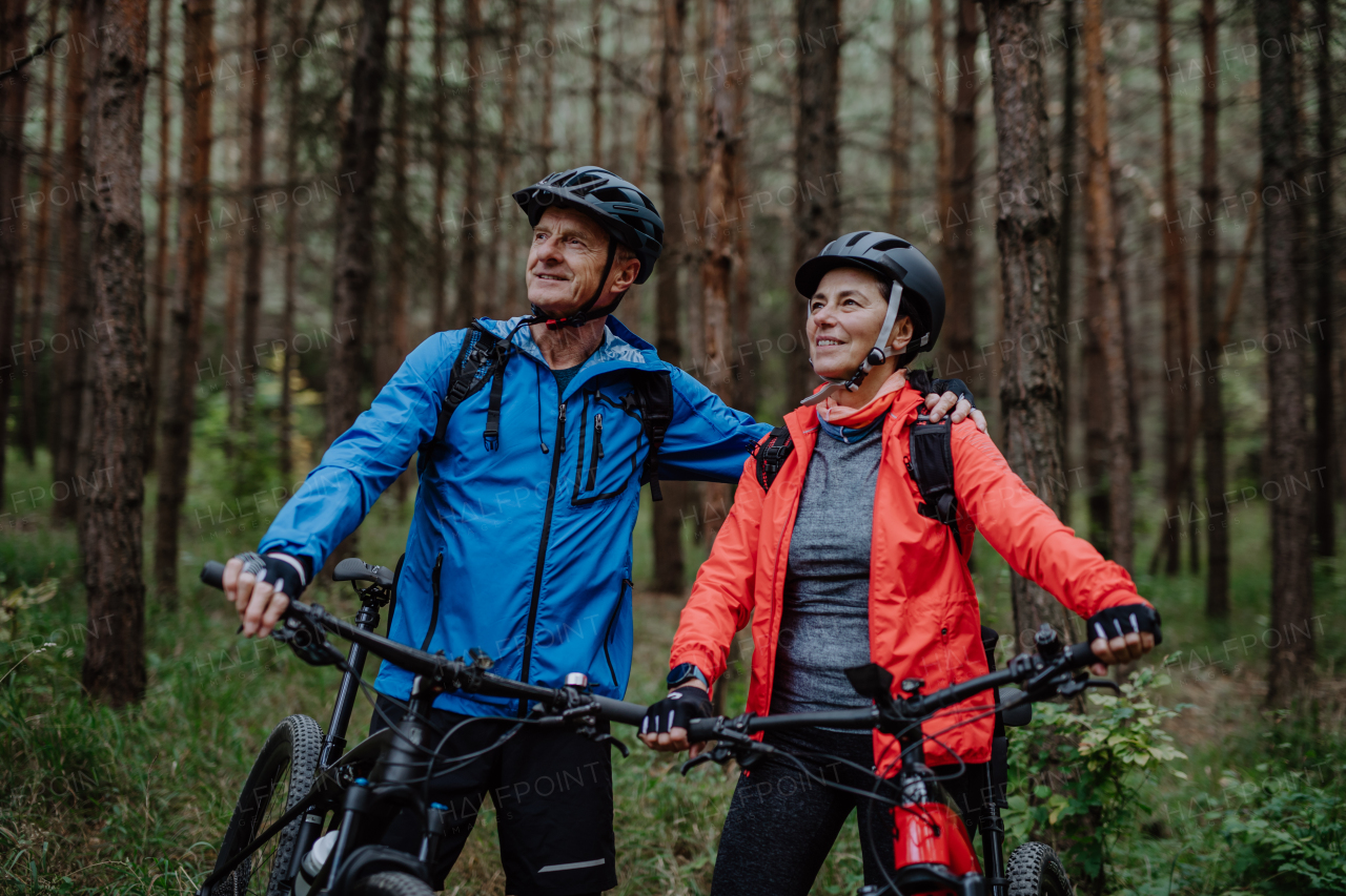 A senior couple bikers with e-bikes admiring nature outdoors in forest in autumn day.