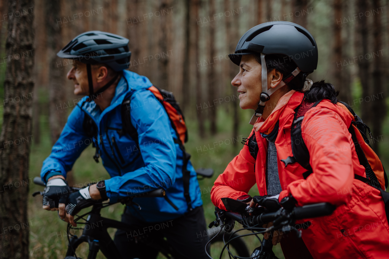 A senior couple bikers with e-bikes admiring nature outdoors in forest in autumn day.