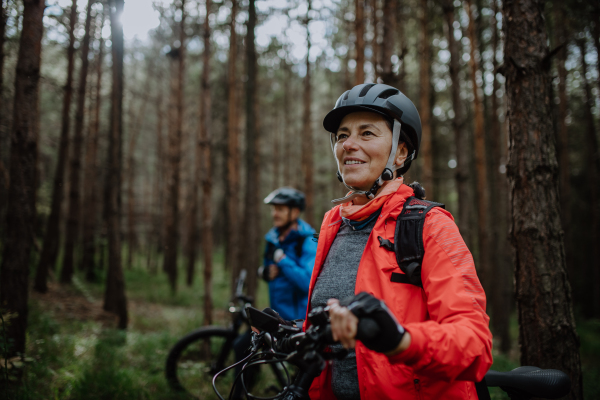 A senior couple bikers with e-bikes admiring nature outdoors in forest in autumn day.