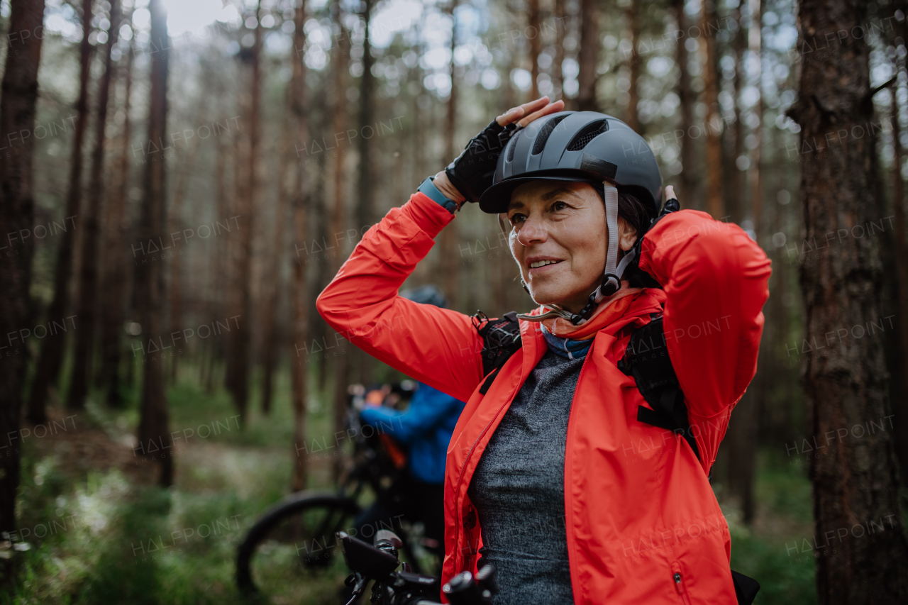 A senior woman biker putting on cycling helmet outdoors in forest in autumn day.