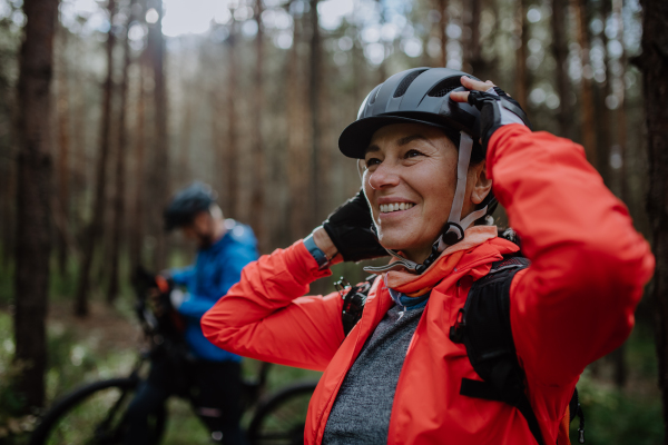 A senior couple bikers putting on cycling helmet outdoors in forest in autumn day.