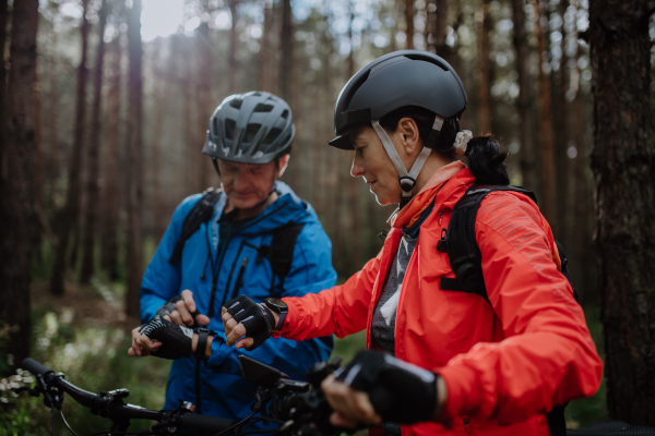 A senior couple bikers setting smartwatch outdoors in forest in autumn day.