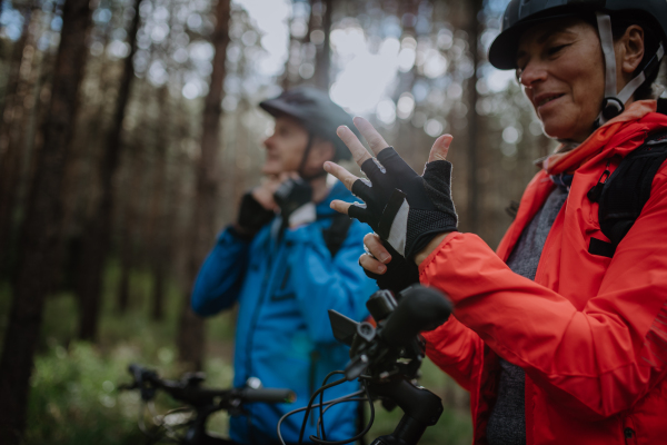 A senior couple bikers putting on cycling helmet and gloves outdoors in forest in autumn day.