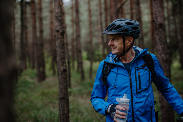 An active senior man biker carrying his bike outdoors in nature in autumn day.