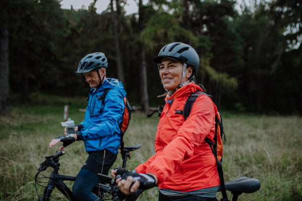 A senior couple bikers with e-bikes admiring nature outdoors in forest in autumn day.