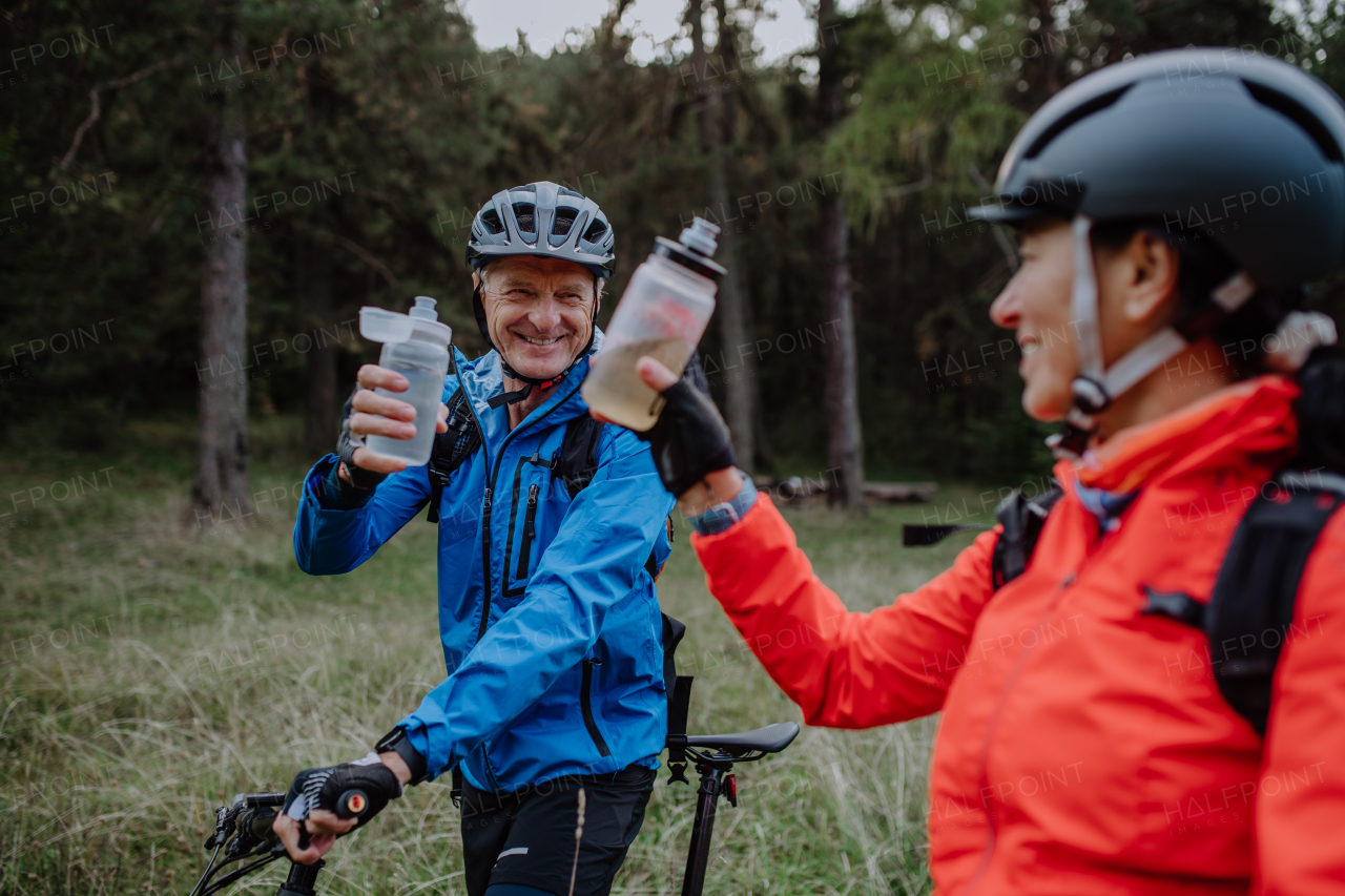 A happy senior couple bikers with wtaer bottles outdoors in forest in autumn day.