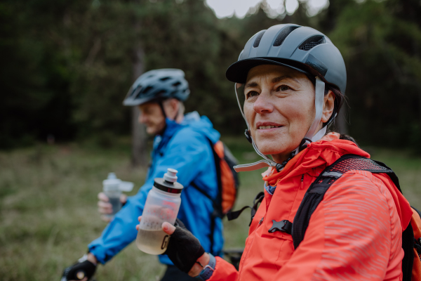 A happy senior couple bikers with water bottles outdoors in forest in autumn day.