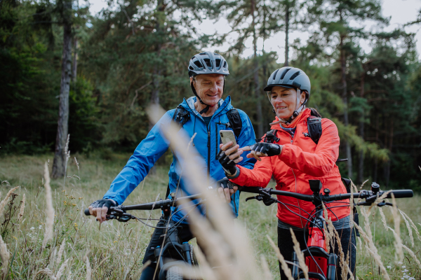 A senior couple bikers using smartphone outdoors in forest in autumn day.