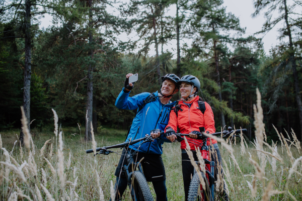 A senior couple bikers using smartphone outdoors in forest in autumn day.