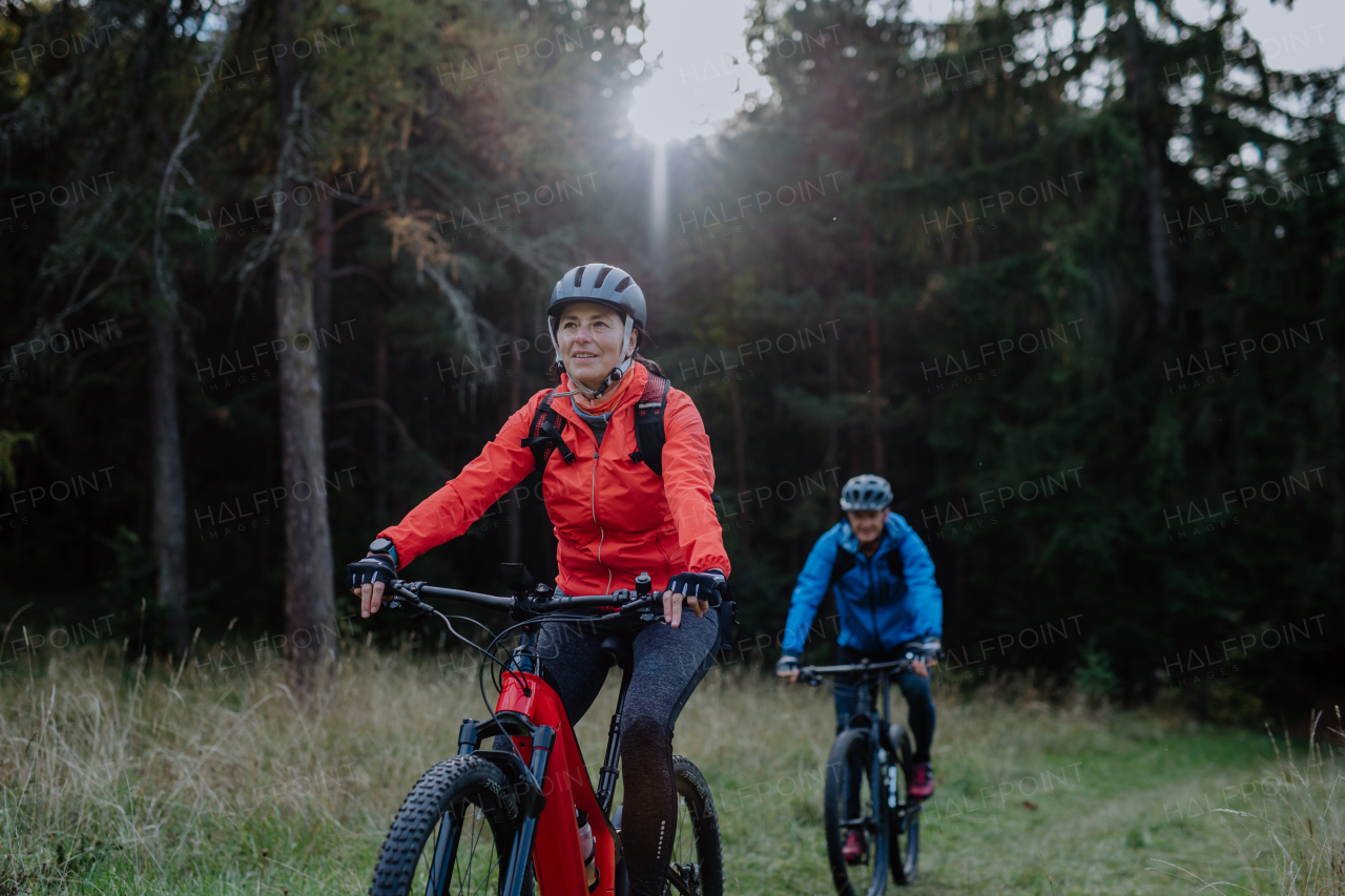 An active senior couple riding bikes outdoors in forest in autumn day.