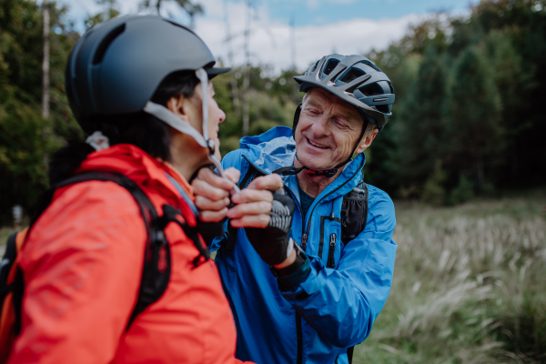 A senior couple bikers putting on cycling helmet outdoors in forest in autumn day.