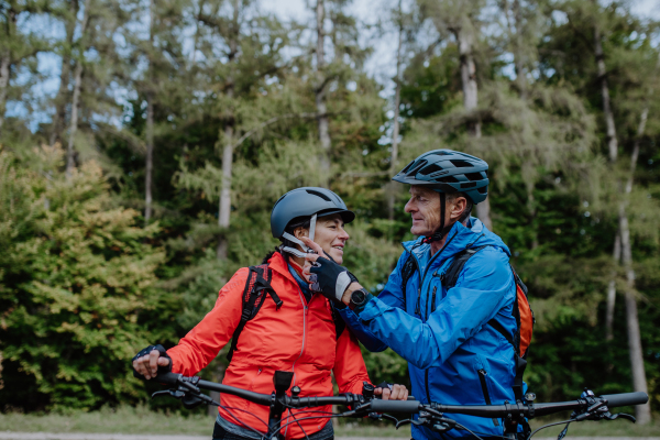 A senior couple bikers putting on cycling helmet outdoors in forest in autumn day.