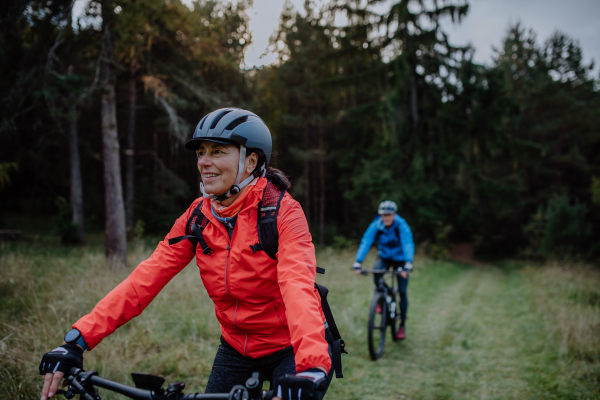 An active senior couple riding bikes outdoors in forest in autumn day.