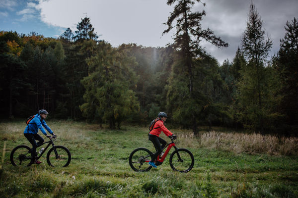 A side view of active senior couple riding bikes outdoors in forest in autumn day.